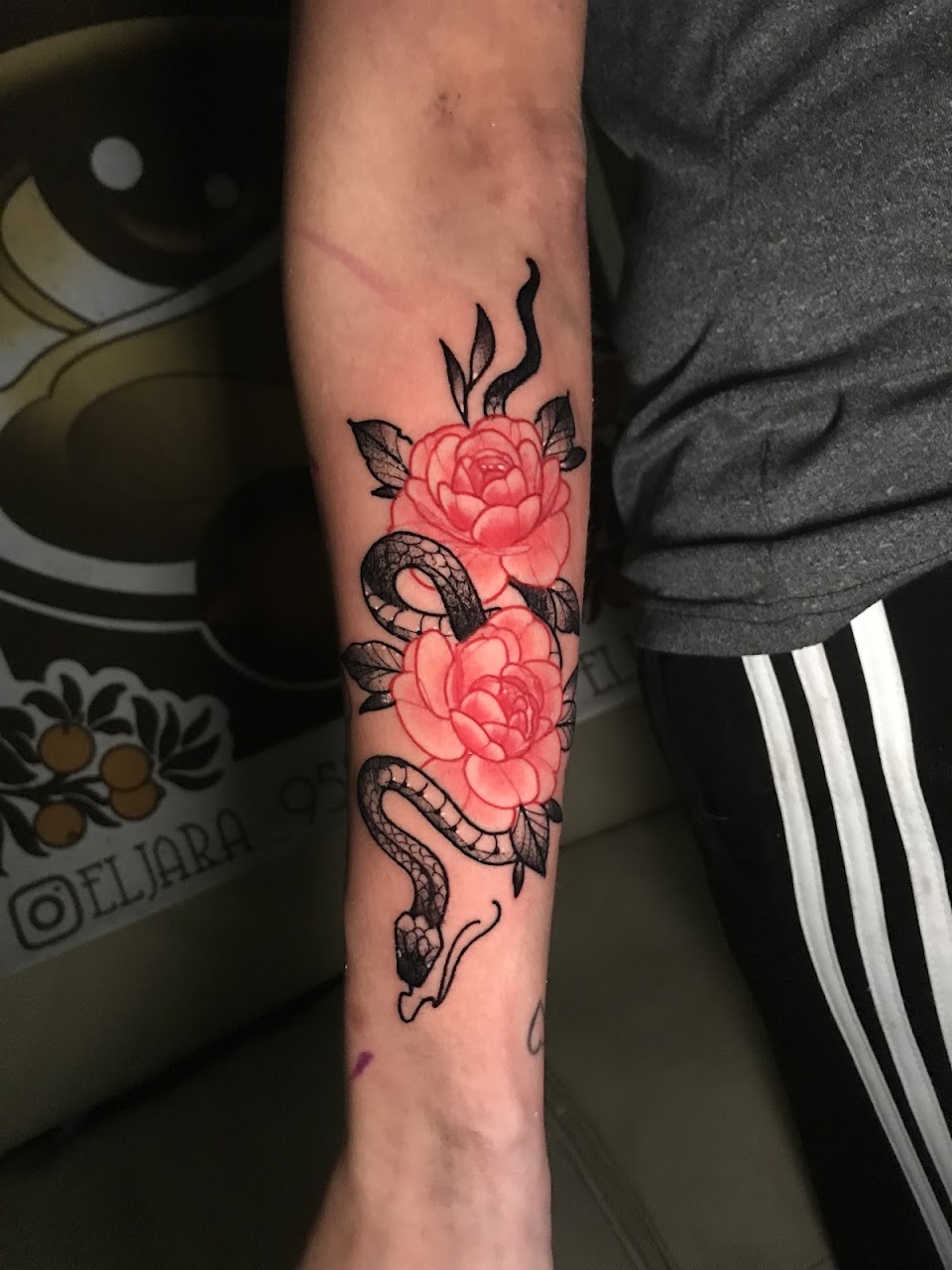 Tatuaje fino botánico con serpiente y flores en antebrazo realizado en El Jara Tattoo Villa Urquiza
